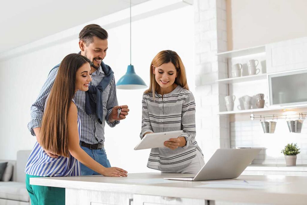 A couple reviews documents with a real estate agent at a table in a cozy, wood-accented home.